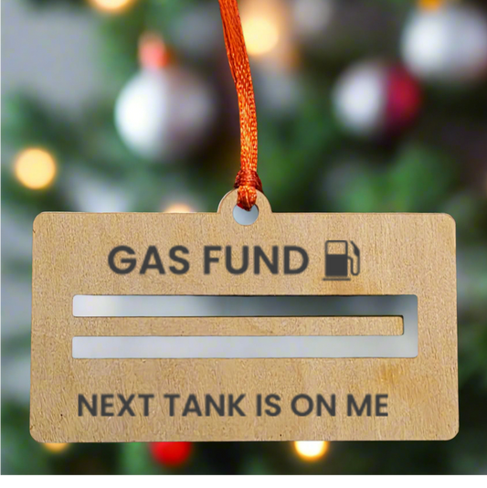 Wooden ornament with 'Gas Fund' text and humorous message against a Christmas tree background