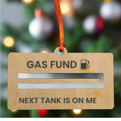 Wooden ornament with 'Gas Fund' text and humorous message against a Christmas tree background